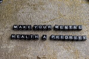 Black lettered blocks on a textured surface spell out, MAKE YOUR MENTAL HEALTH A PRIORITY..